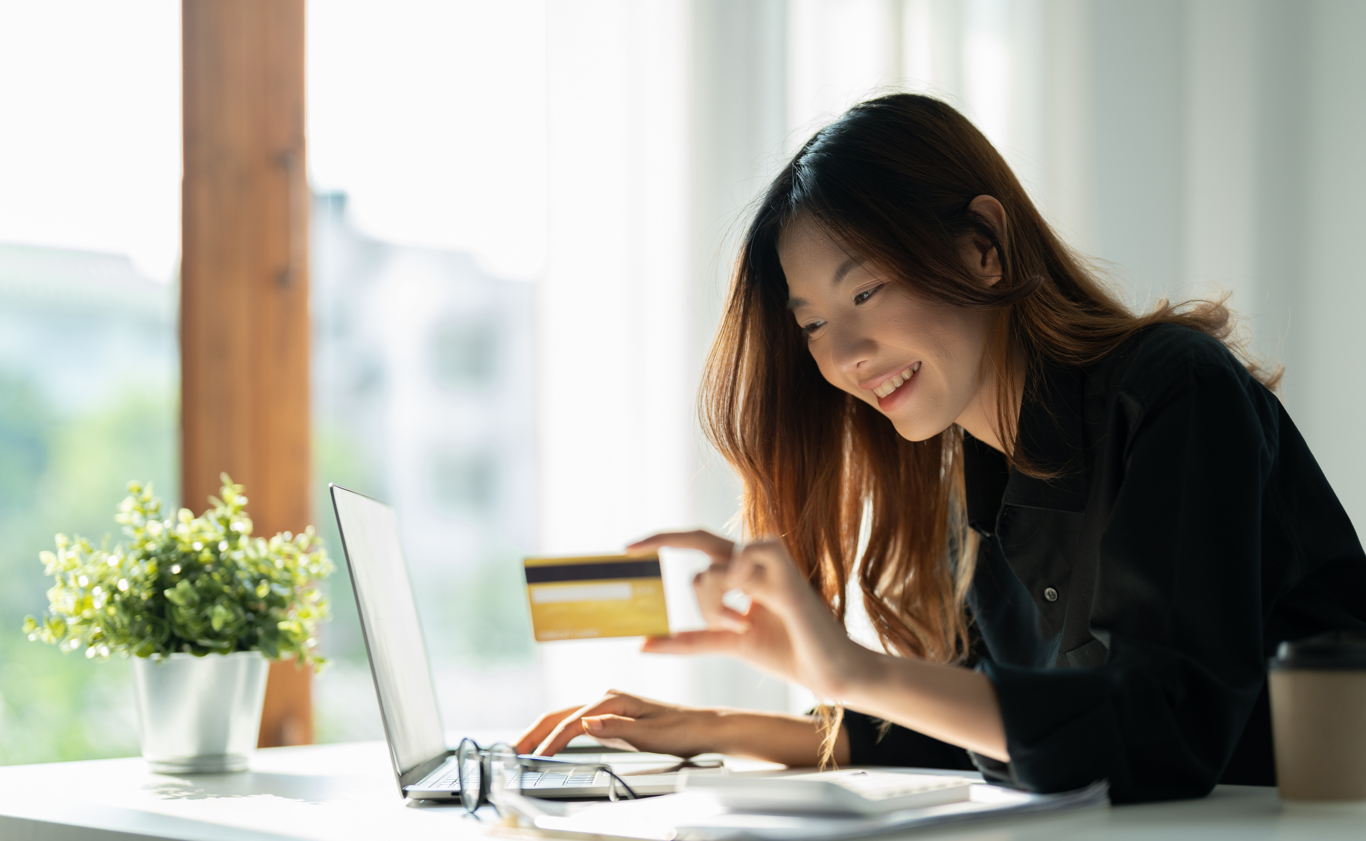Happy woman holding credit card and using laptop computer fo